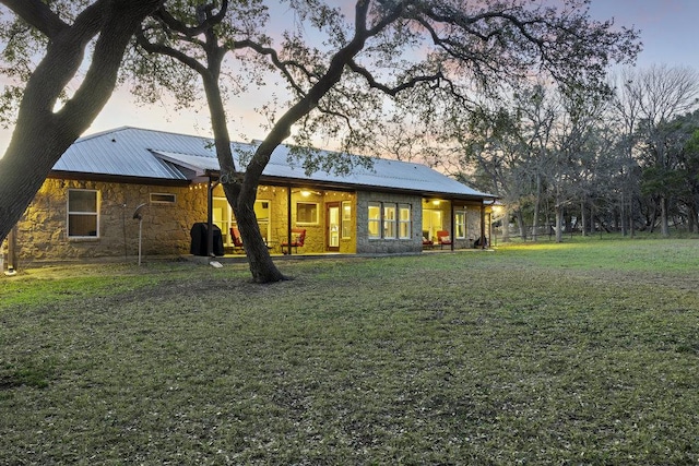 back of property at dusk featuring metal roof, stone siding, and a lawn