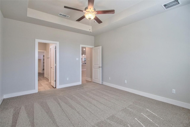 121 Pinnacle Ln, Kyle, TX 78640 - unfurnished bedroom featuring a raised ceiling, light colored carpet, baseboards, connected bathroom, and a ceiling fan