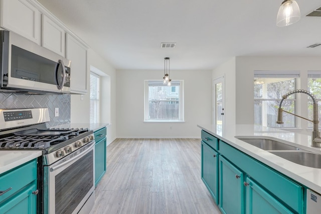 kitchen featuring tasteful backsplash, appliances with stainless steel finishes, blue cabinetry, pendant lighting, and a sink