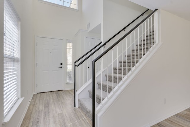 entryway featuring baseboards, a high ceiling, stairs, and light wood-style floors