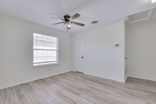 unfurnished room featuring visible vents, light wood-style floors, attic access, a ceiling fan, and baseboards