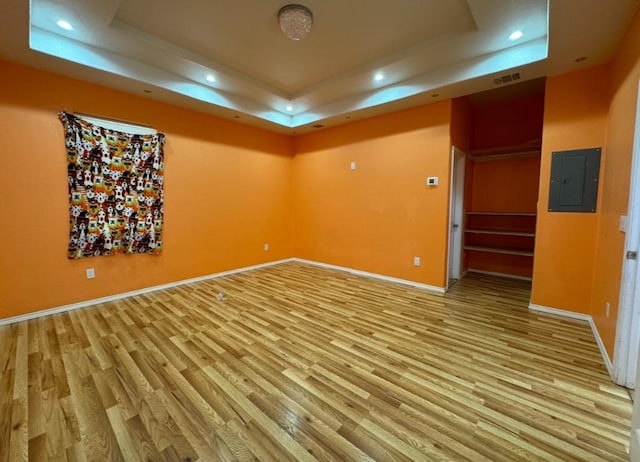 unfurnished room with light wood finished floors, electric panel, visible vents, a raised ceiling, and recessed lighting