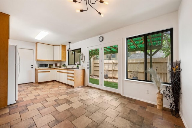 kitchen with light countertops, stainless steel microwave, freestanding refrigerator, and baseboards