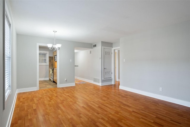 empty room featuring a chandelier, a healthy amount of sunlight, light wood-type flooring, and baseboards