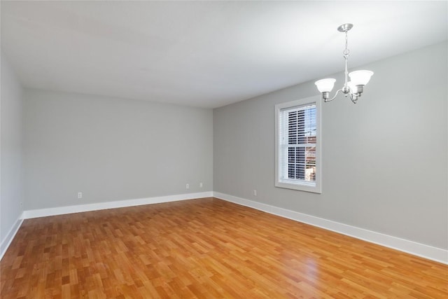 unfurnished room featuring baseboards, light wood finished floors, and a chandelier