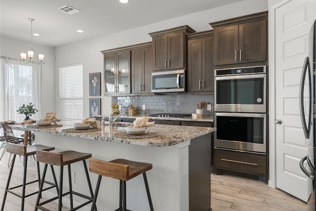 kitchen with a breakfast bar area, stainless steel appliances, visible vents, dark brown cabinets, and decorative backsplash