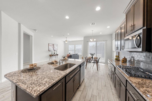 kitchen featuring light wood-style flooring, dark brown cabinetry, a sink, appliances with stainless steel finishes, and backsplash