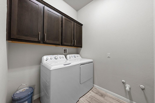 washroom featuring light wood finished floors, washer and clothes dryer, cabinet space, and baseboards