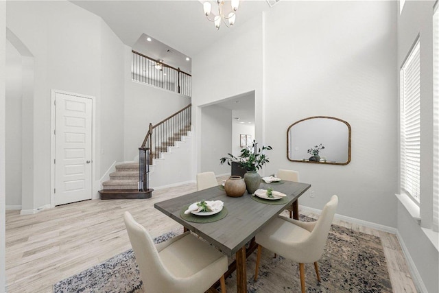 dining space featuring a notable chandelier, stairway, a towering ceiling, wood finished floors, and baseboards