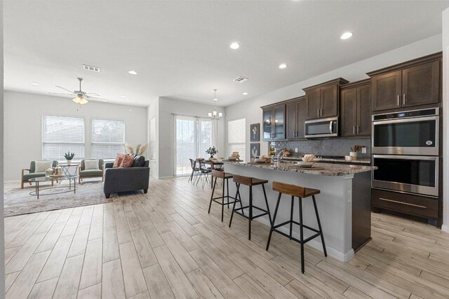 kitchen featuring a kitchen breakfast bar, visible vents, stainless steel appliances, light wood finished floors, and backsplash