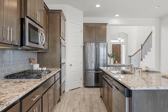 kitchen with stainless steel appliances, a sink, dark brown cabinets, light wood finished floors, and an island with sink