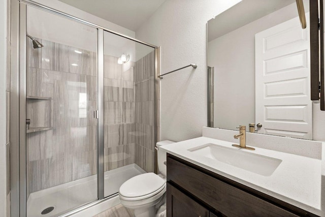 bathroom featuring toilet, a stall shower, a textured wall, and vanity