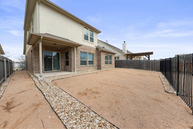 back of property featuring brick siding, stucco siding, a patio area, a pergola, and a fenced backyard