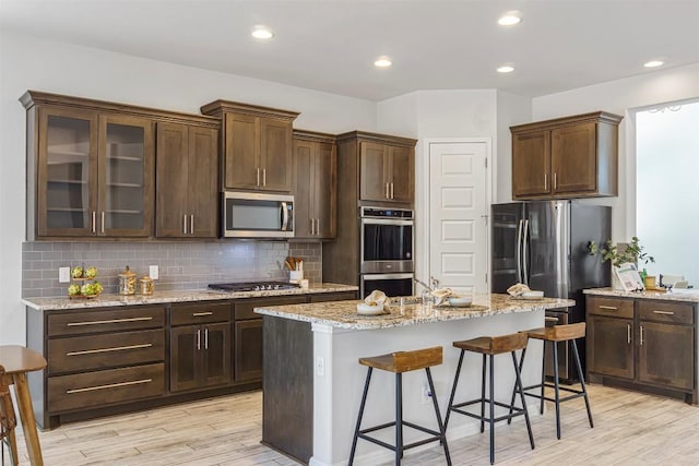kitchen featuring light wood-type flooring, appliances with stainless steel finishes, a kitchen bar, backsplash, and a kitchen island