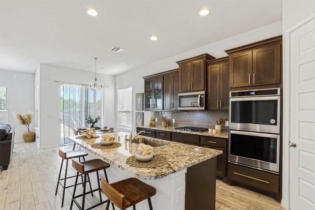 kitchen with dark brown cabinetry, a breakfast bar, light stone counters, appliances with stainless steel finishes, and a sink