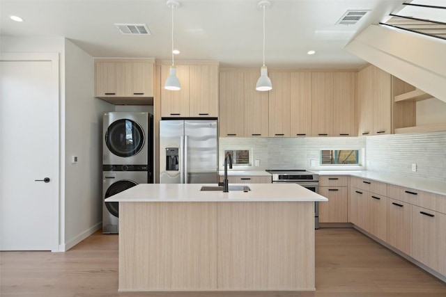 kitchen with visible vents, appliances with stainless steel finishes, stacked washing maching and dryer, light brown cabinets, and a sink