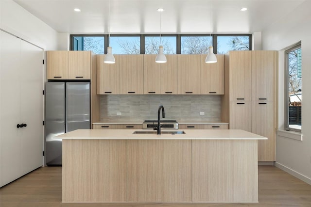 kitchen with modern cabinets, freestanding refrigerator, a sink, light brown cabinets, and backsplash