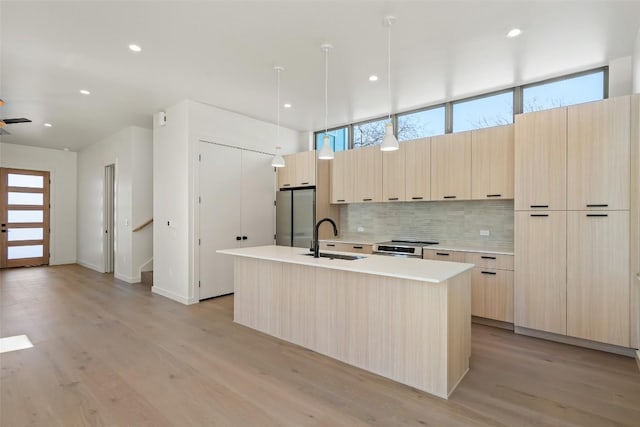 kitchen featuring tasteful backsplash, modern cabinets, freestanding refrigerator, light brown cabinetry, and a sink