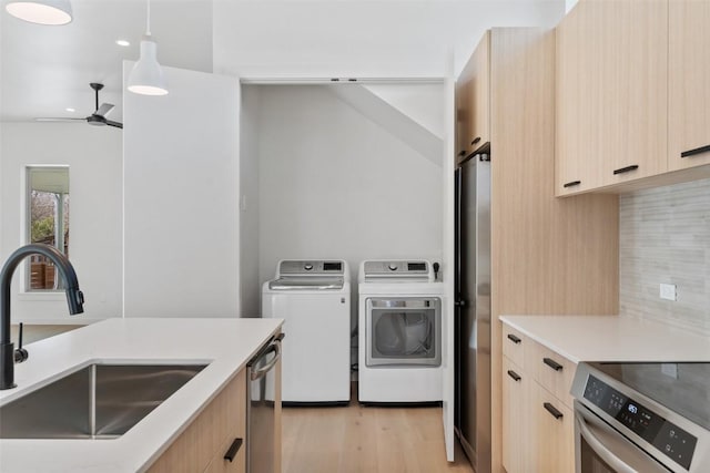 kitchen featuring modern cabinets, appliances with stainless steel finishes, washer and dryer, light brown cabinetry, and a sink