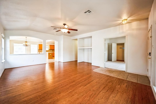 unfurnished living room with visible vents, arched walkways, light wood-style flooring, and ceiling fan with notable chandelier