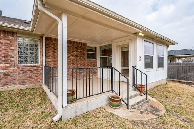 doorway to property featuring brick siding and fence