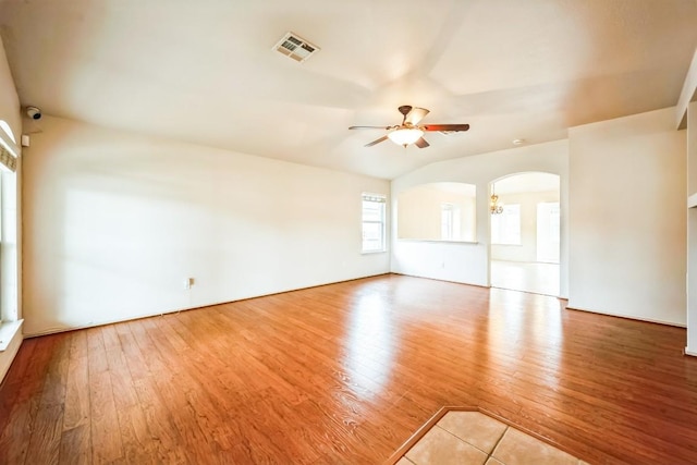 empty room featuring visible vents, wood finished floors, arched walkways, ceiling fan, and vaulted ceiling