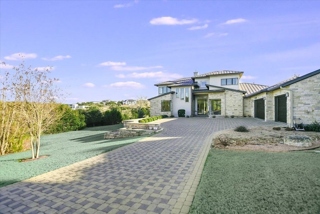 back of house featuring stone siding, metal roof, decorative driveway, and a standing seam roof