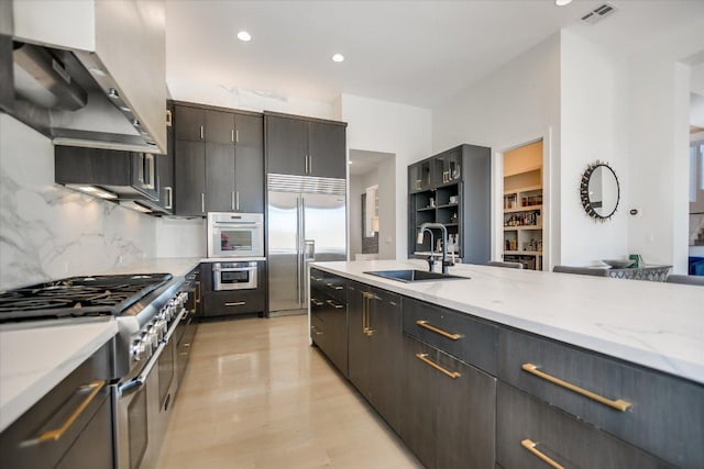 kitchen featuring visible vents, a sink, wall chimney range hood, light wood finished floors, and high end appliances