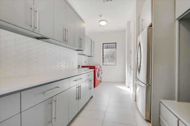 kitchen featuring light countertops, light tile patterned floors, decorative backsplash, freestanding refrigerator, and separate washer and dryer