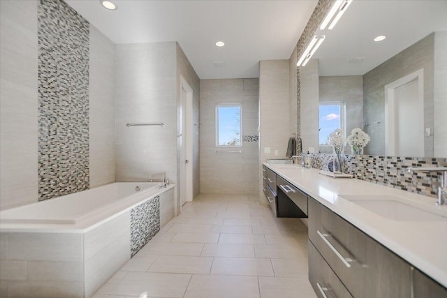 bathroom featuring tile patterned flooring, decorative backsplash, a bath, tile walls, and a sink