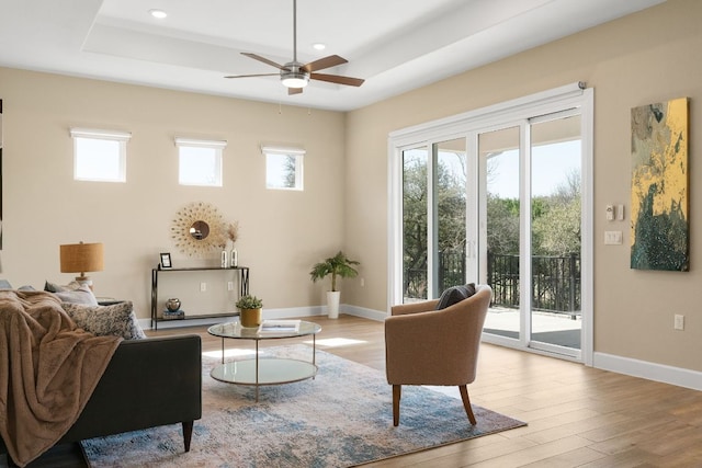 living area with wood finished floors, a raised ceiling, and a healthy amount of sunlight