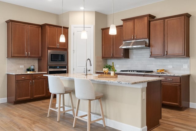 kitchen featuring a breakfast bar area, stainless steel appliances, a kitchen island with sink, light wood-type flooring, and under cabinet range hood