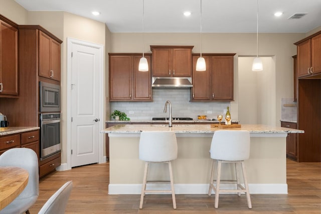 kitchen featuring stainless steel appliances, light wood-style floors, visible vents, and under cabinet range hood