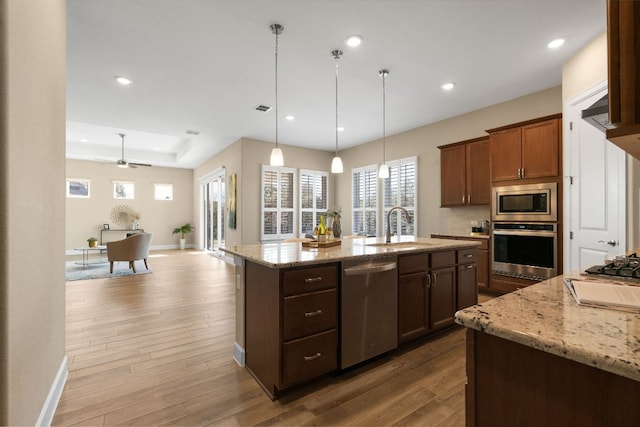 kitchen with wood finished floors, light stone countertops, a kitchen island with sink, stainless steel appliances, and a sink