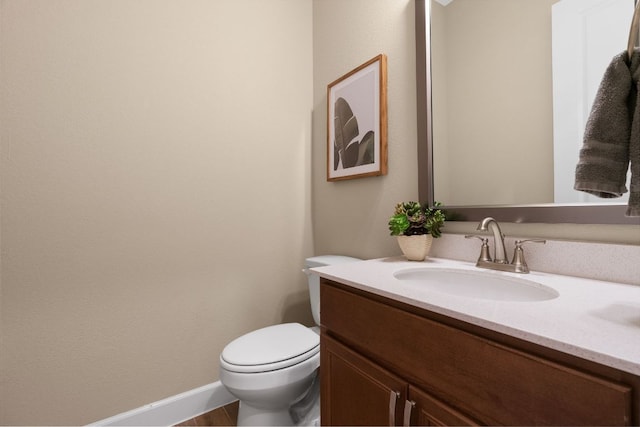 half bath featuring baseboards, vanity, and toilet