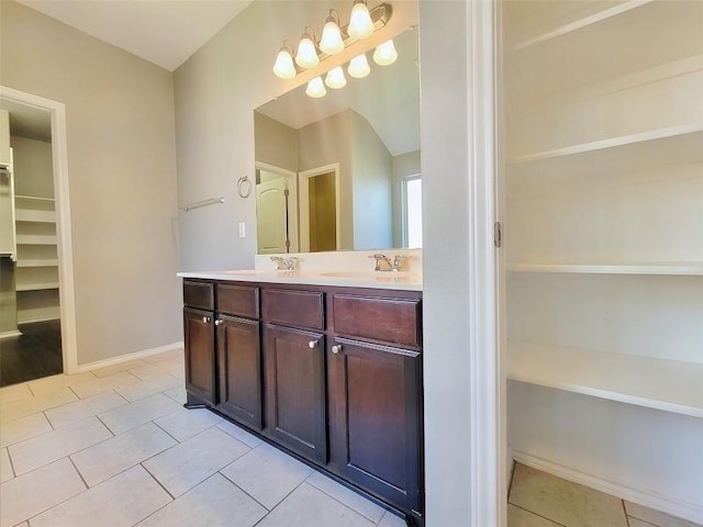 bathroom featuring a sink, baseboards, tile patterned floors, double vanity, and a walk in closet