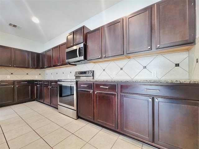 kitchen featuring light tile patterned floors, light stone countertops, stainless steel appliances, visible vents, and decorative backsplash