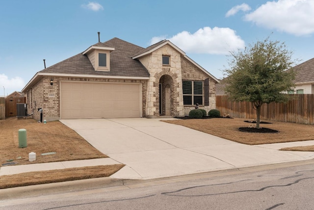 french country inspired facade featuring a garage, central AC, fence, stone siding, and concrete driveway