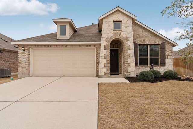 view of front of house featuring an attached garage, central air condition unit, fence, stone siding, and concrete driveway