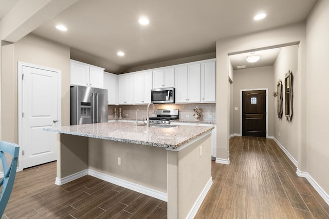 kitchen with dark wood-style floors, a center island with sink, stainless steel appliances, backsplash, and white cabinetry