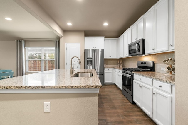 kitchen featuring appliances with stainless steel finishes, a center island with sink, a sink, and decorative backsplash