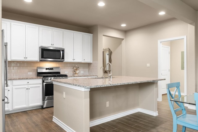 kitchen featuring an island with sink, decorative backsplash, stainless steel appliances, and dark wood-style flooring