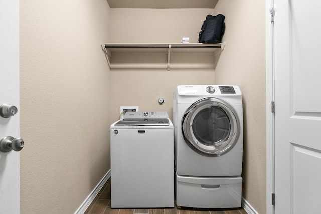 clothes washing area with laundry area, separate washer and dryer, wood tiled floor, and baseboards