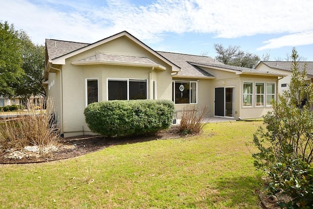 rear view of property with a shingled roof, a lawn, and stucco siding