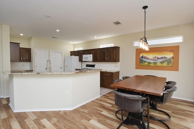 kitchen featuring dark brown cabinetry, white appliances, light wood-style floors, and a sink