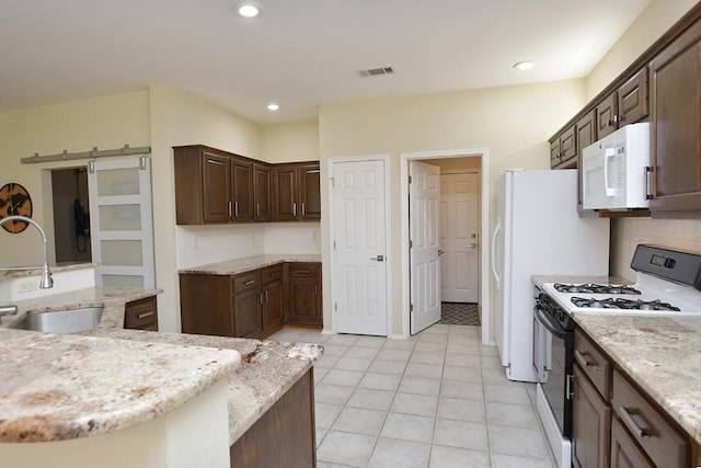 kitchen featuring recessed lighting, visible vents, a barn door, a sink, and white appliances