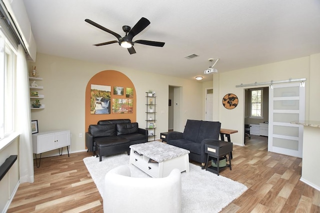 living area with ceiling fan, a barn door, visible vents, baseboards, and light wood-style floors