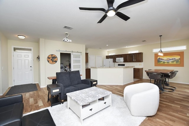 living room featuring a barn door, visible vents, baseboards, a ceiling fan, and light wood-type flooring