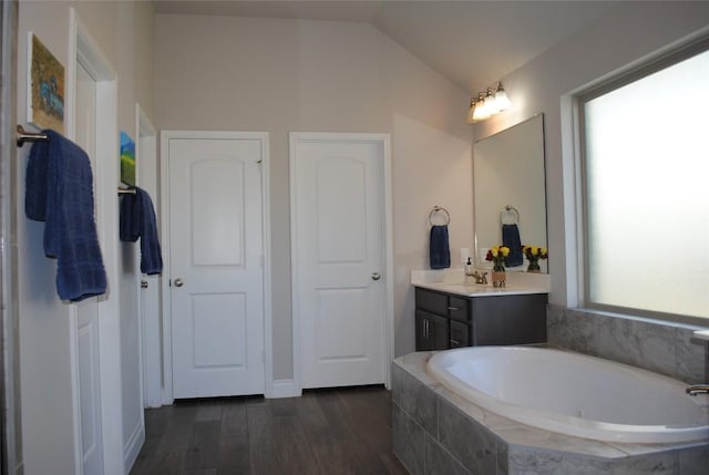 bathroom with lofted ceiling, wood finished floors, vanity, and a bath