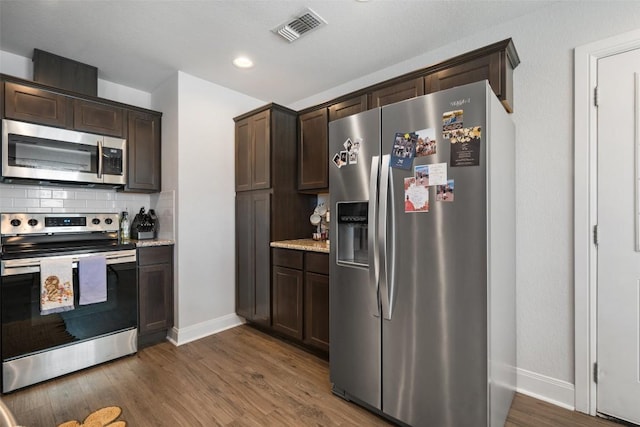 kitchen with visible vents, wood finished floors, dark brown cabinetry, appliances with stainless steel finishes, and decorative backsplash